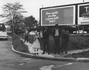 Untitled [Spectators on street corner in front of billboard]